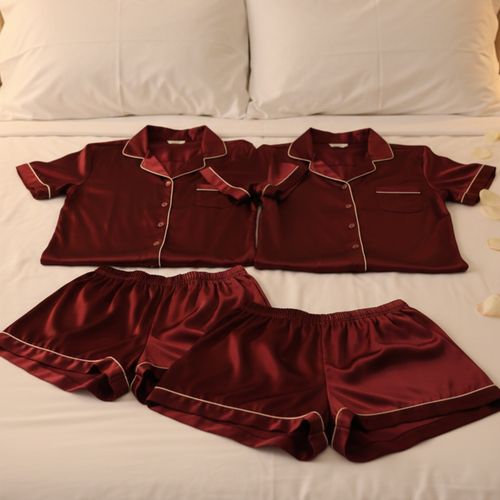 Couple silk pajama set displayed on a bed, featuring matching shirts and shorts in a rich burgundy color.